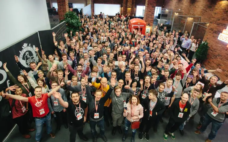 Group of conference attendees indoors, smiling and waving at the camera with name tags